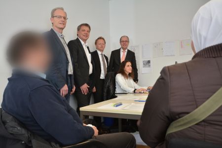 Betty Atlassi (sitzend) bearbeitet den Asylantrag von einem Flüchtlingsehepaar, dahinter: Gerhard Kruse (Teamleiter der Ausländerbehörde), Horst-Hermann Müller (Geschäftsführer des Jobcenters), Volker Mäulen (Leiter der BAMF Außenstelle in Bielefeld) und Landrat Manfred Müller. 
